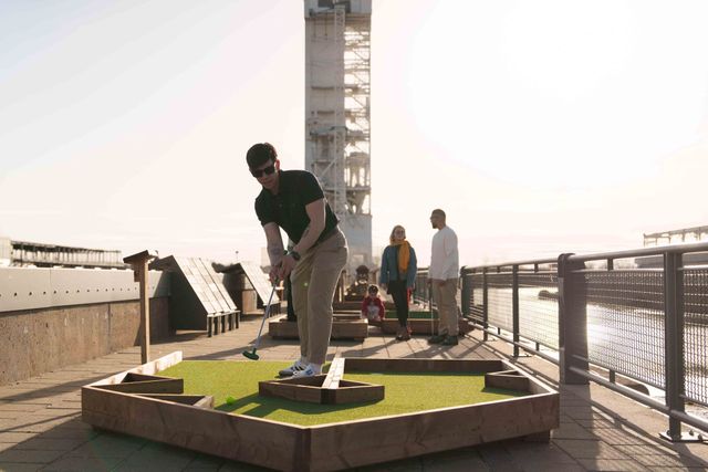 Une personne jouant au mini-golf près d'une rambarde au coucher du soleil