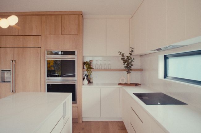 Cuisine moderne avec placards en bois clair, comptoirs blancs et plaque de cuisson noire près d'une fenêtre