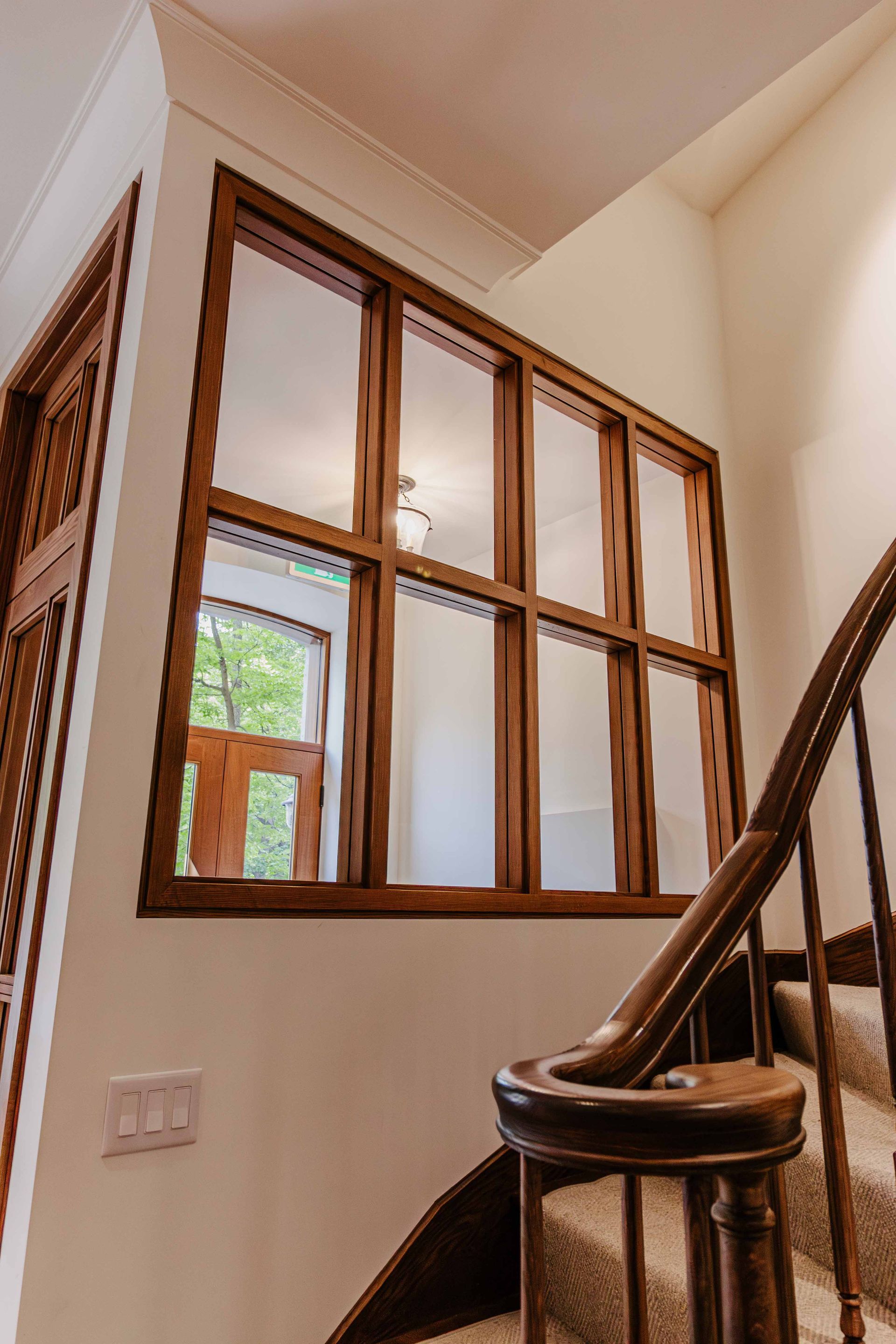 Palier d'escalier avec rampe en bois et mur vitré donnant sur un couloir intérieur beige