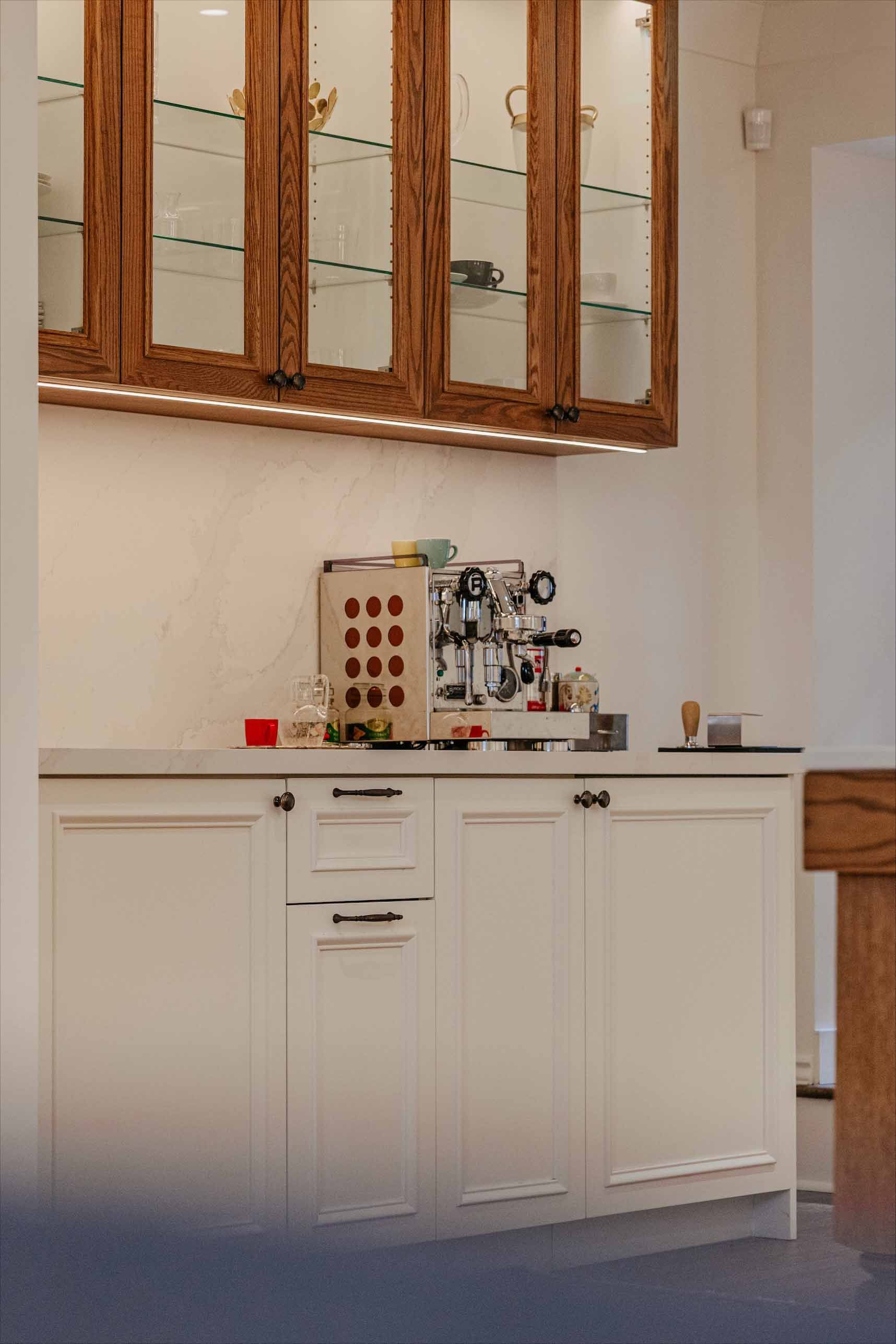 Meuble de cuisine blanc avec appareils électroménagers intégrés sous une fenêtre à volets en bois