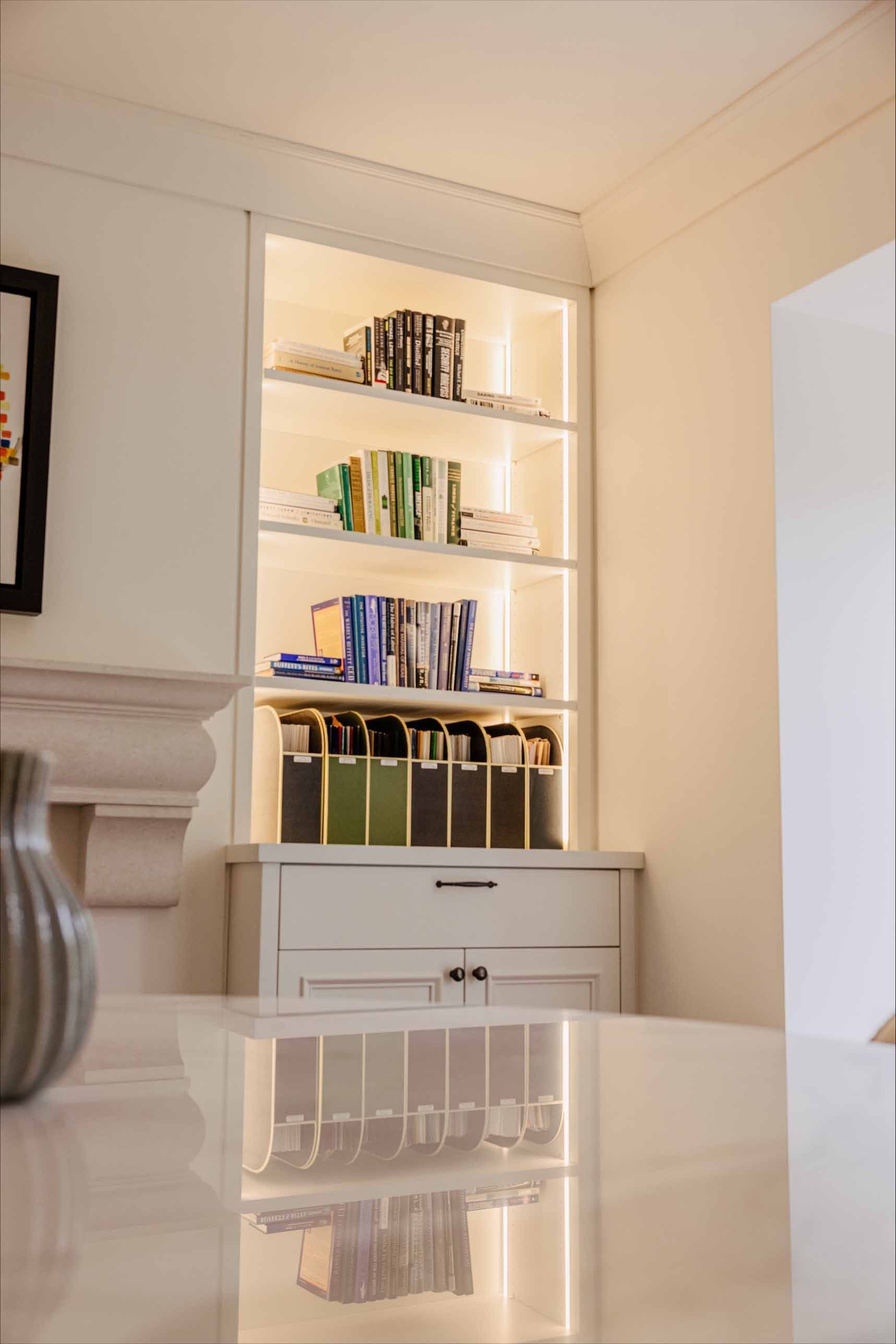 Bibliothèque blanche encastrée avec livres et objets de décoration dans une pièce lumineuse, se reflétant sur une table brillante