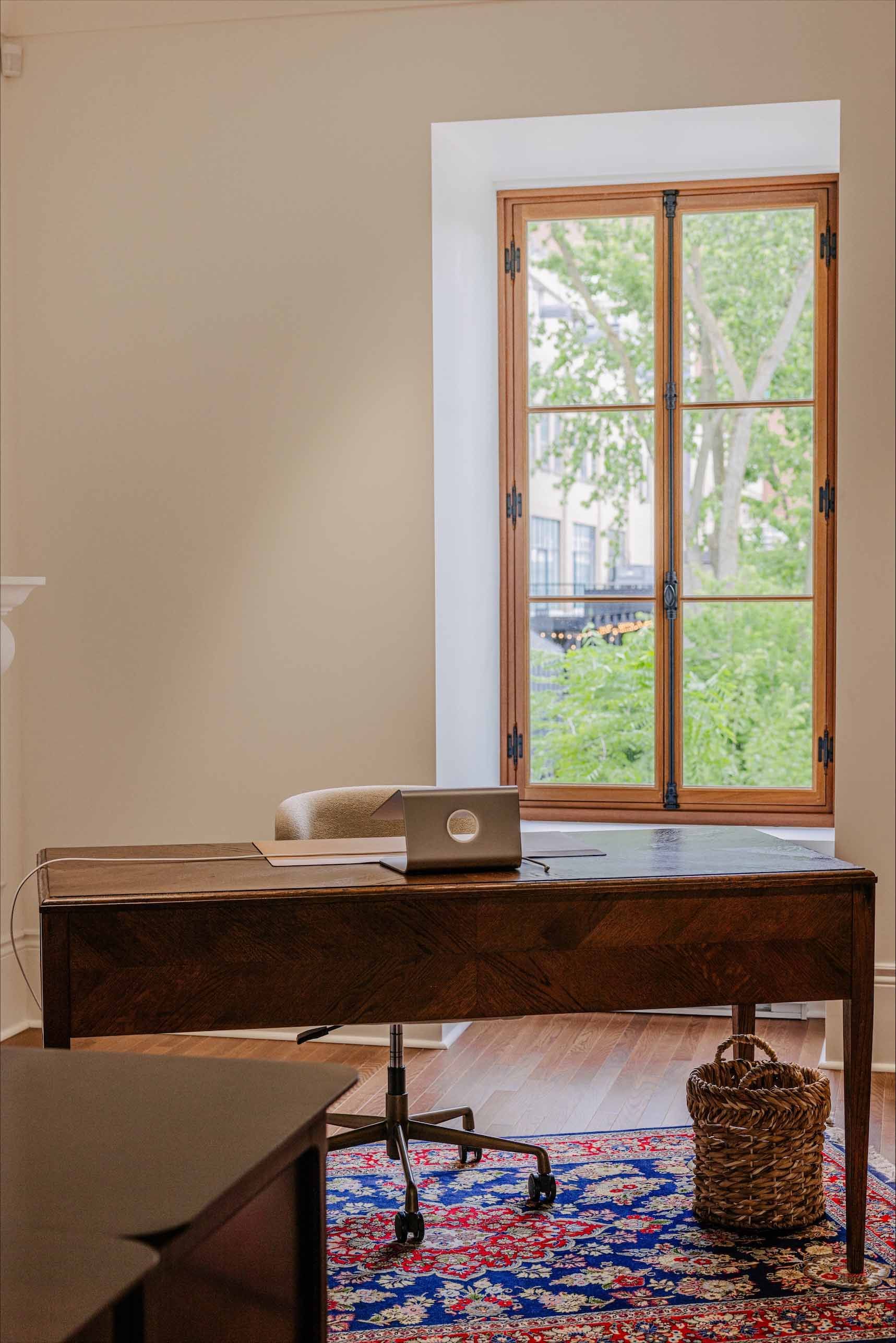 Bureau à domicile près d'une fenêtre avec un ordinateur portable, une chaise et un tapis coloré