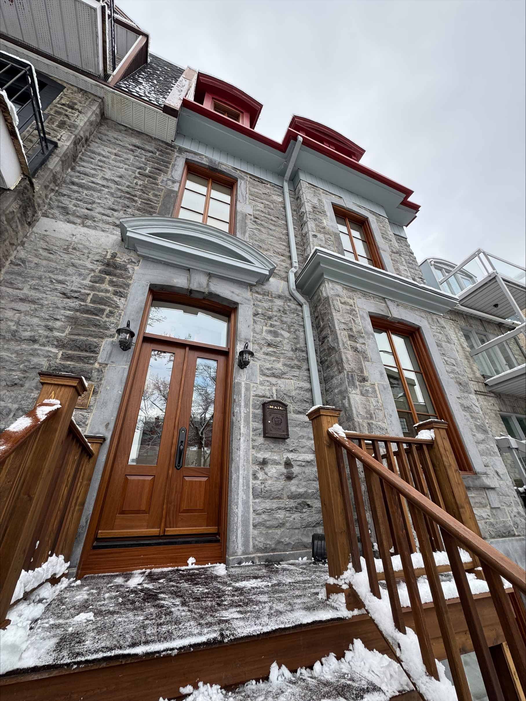 Maison de ville en pierre enneigée avec porte et escalier en bois, vue d'en bas