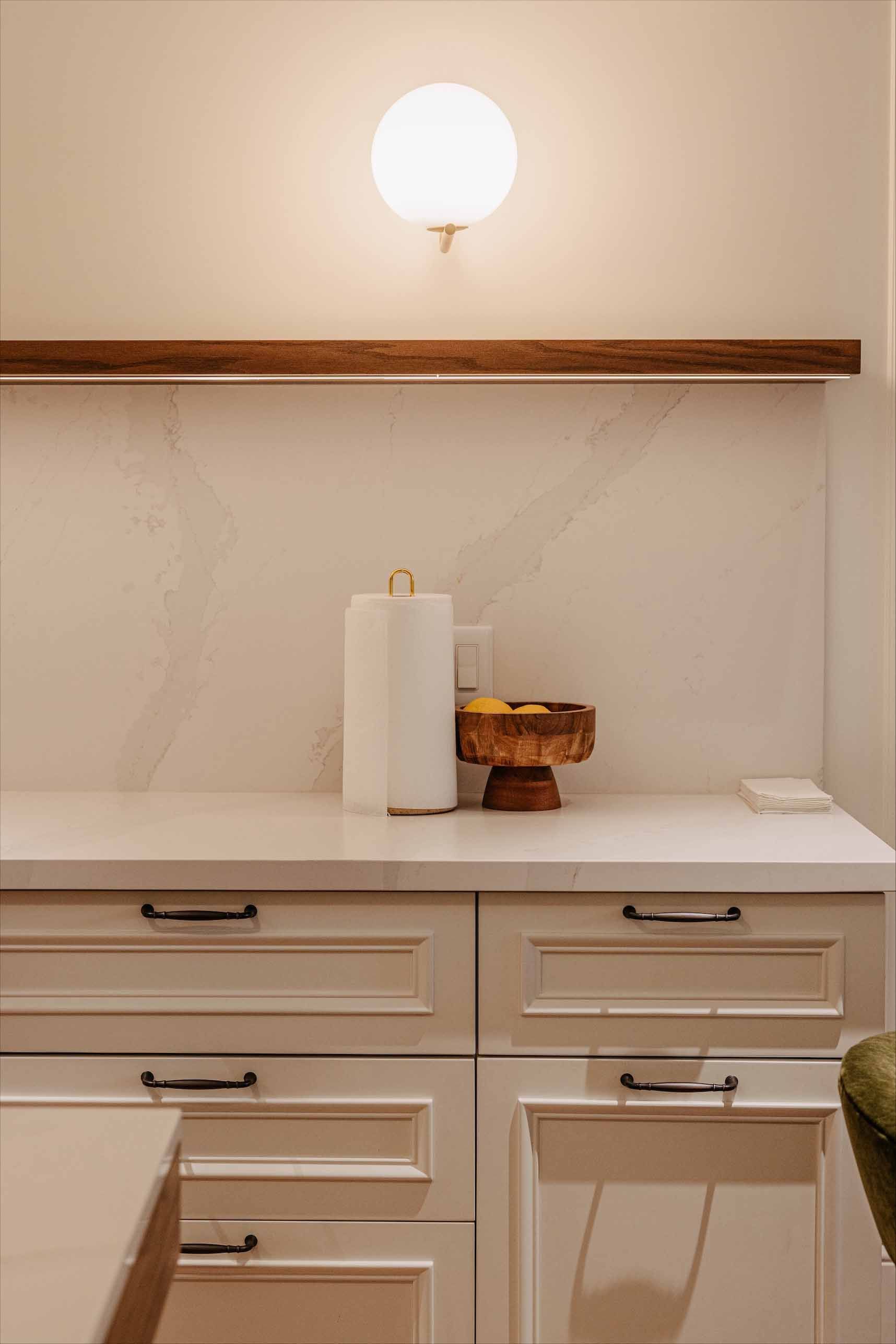 Meuble-lavabo minimaliste avec comptoir blanc, tiroirs, applique murale, porte-essuie-tout et petits objets de décoration