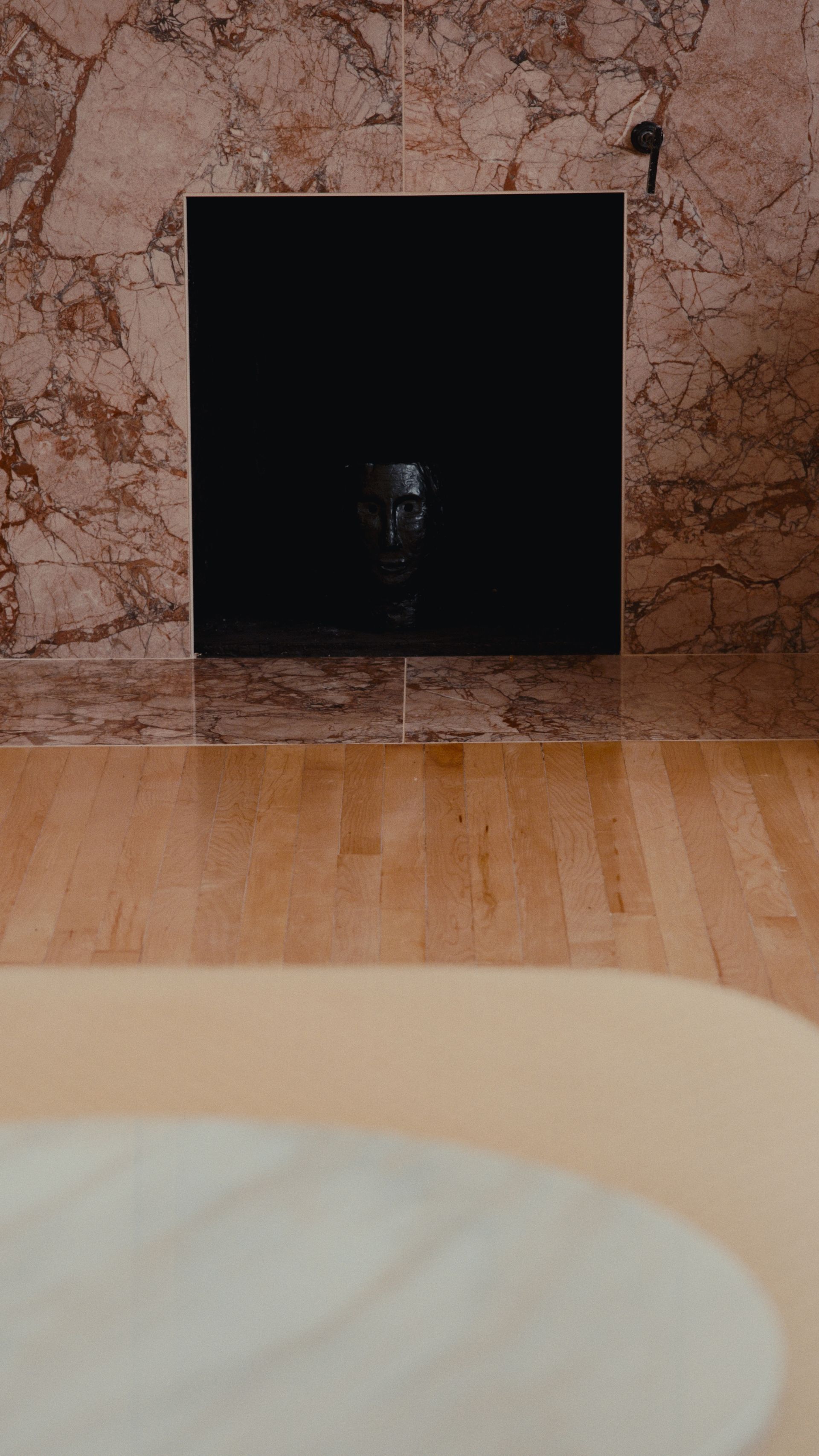 Cheminée noire encastrée dans un mur de marbre, au-dessus d'un parquet clair.