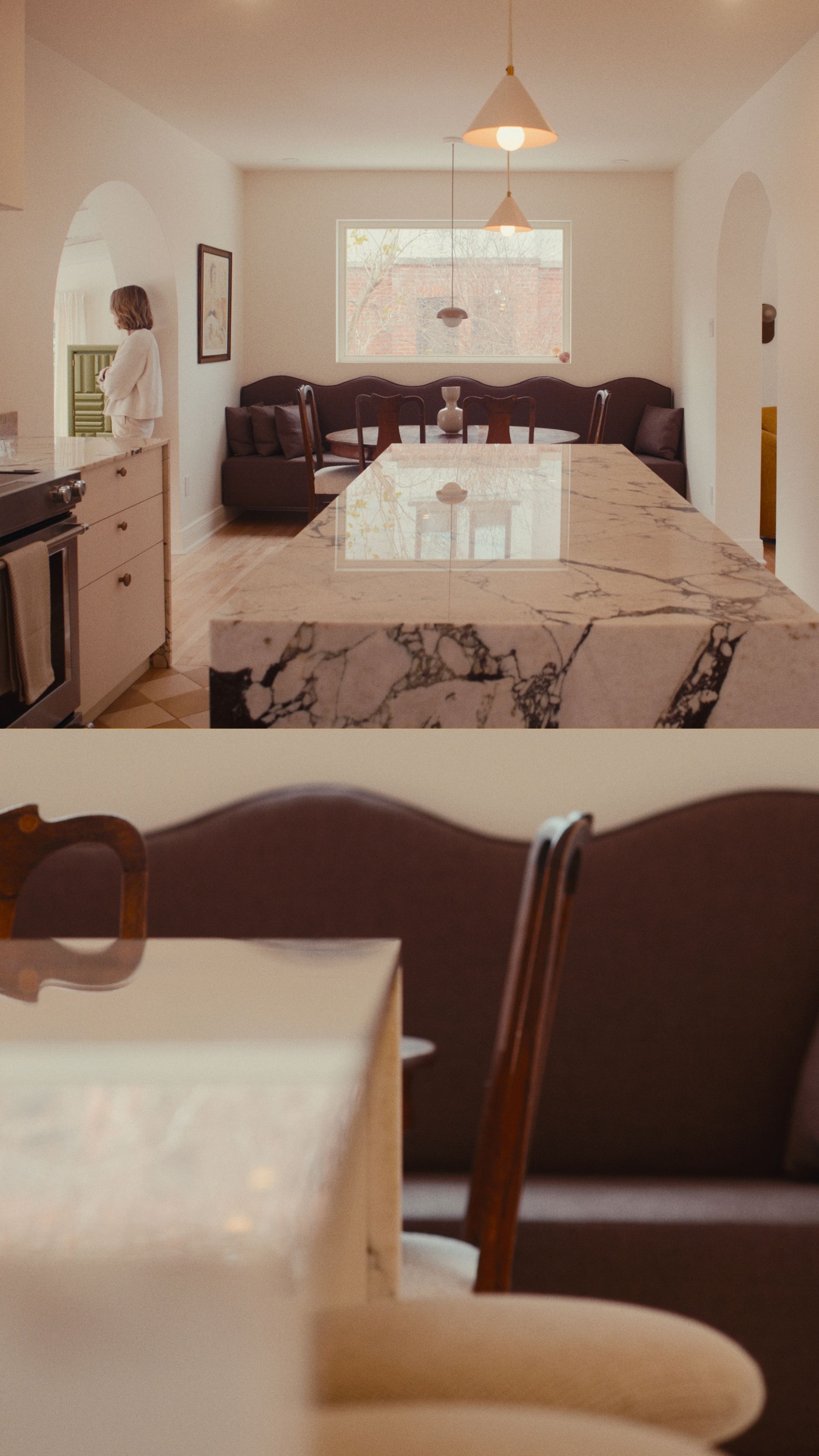 Longue cuisine avec un îlot en marbre, une table à manger et une personne dans la cuisine.