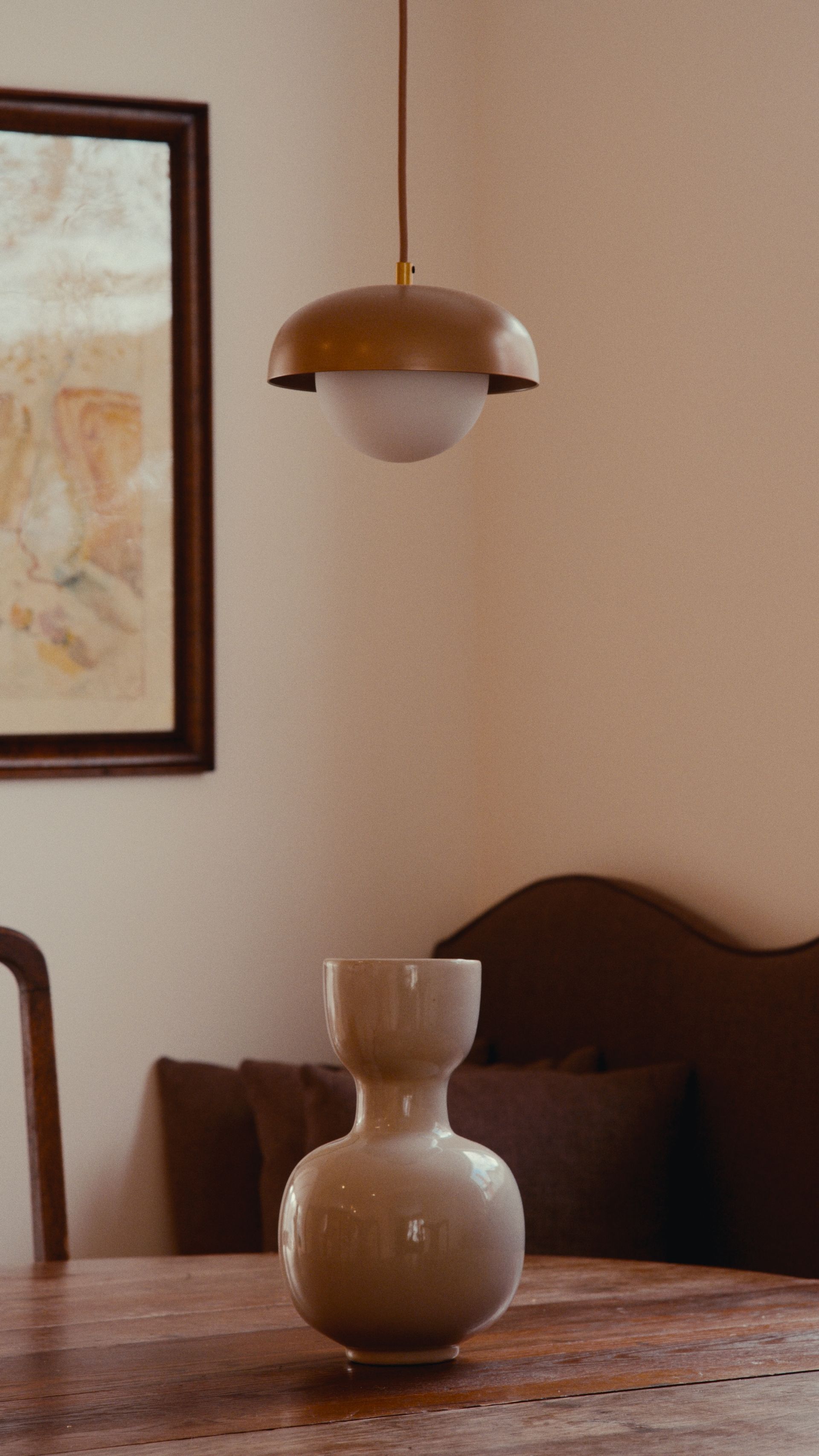 Scène de salle à manger. Suspension en laiton au-dessus d'une table en bois avec un vase. Un tableau encadré est accroché au mur.