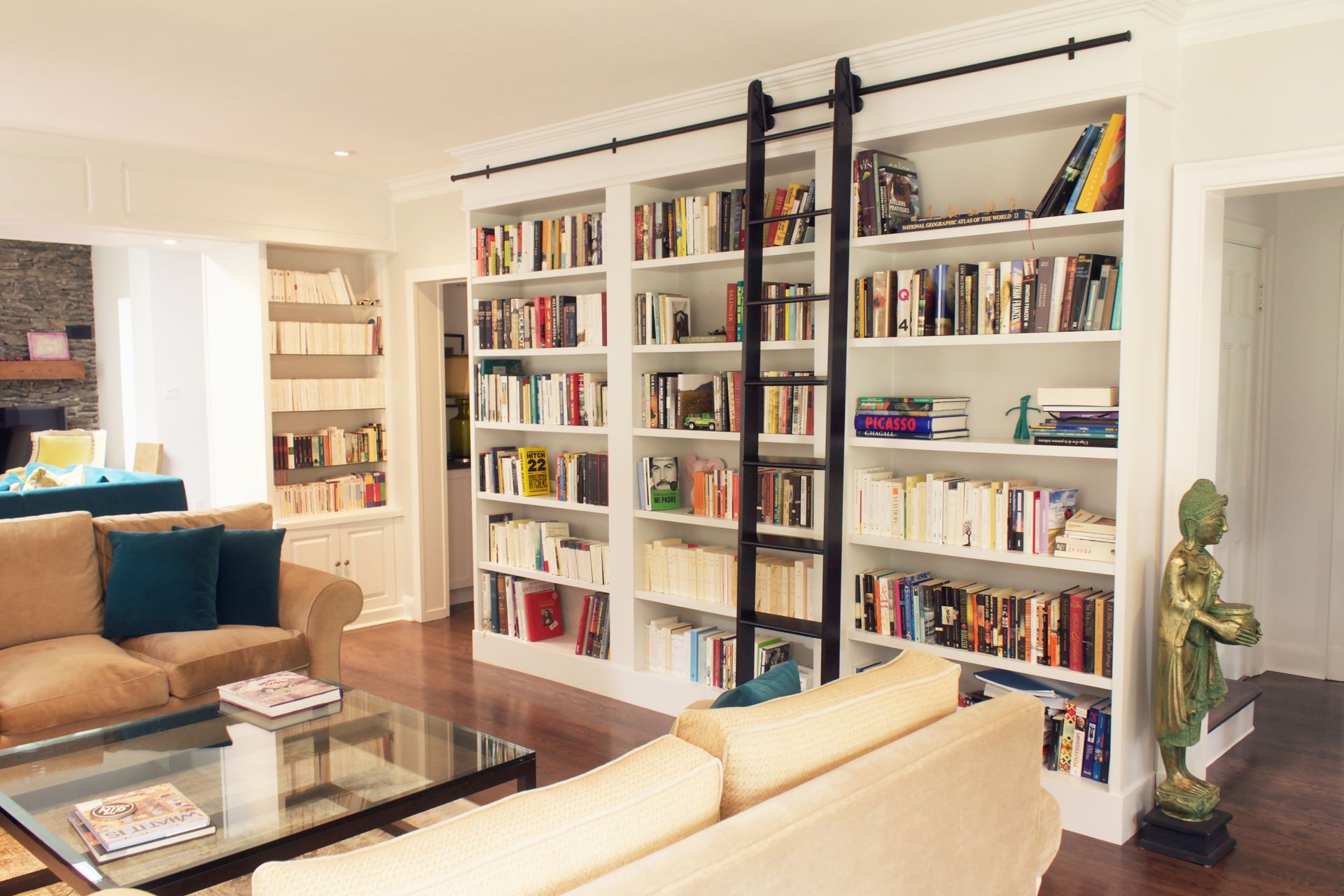 Salon avec bibliothèque intégrée, échelle roulante, canapés et table basse en verre.