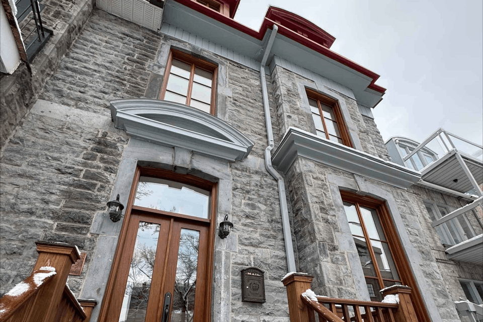 Façade en pierre d'une maison avec portes en bois, grandes fenêtres et ornements de toit rouges, vue d'en bas
