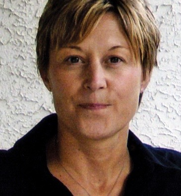 Woman with short, blonde hair, facing forward. Wearing a black shirt, neutral background.