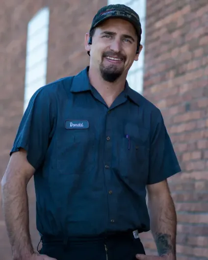 Man in navy work uniform and cap standing outdoors beside a brick wall, smiling at the camera. Man in navy work uniform and cap standing outdoors beside a brick wall, smiling at the camera.