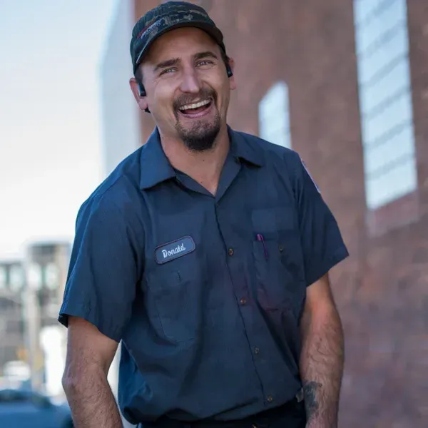 Smiling worker in a dark blue uniform and cap standing outdoors near a brick building. Smiling worker in a dark blue uniform and cap standing outdoors near a brick building.