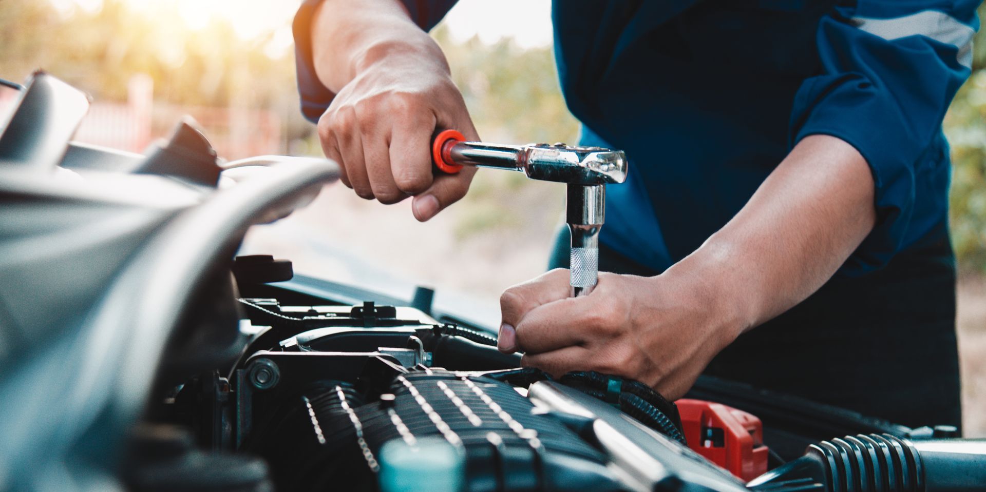 Smiling worker in a dark blue uniform standing beside a brick building Mechanic using a wrench to repair a car engine in a garage