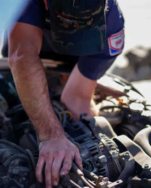 Mechanic in blue shirt inspecting a car engine with hands on hoses and components Mechanic in blue shirt inspecting a car engine with hands on hoses and components