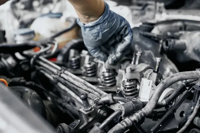 Mechanic’s gloved hand working on a car engine with exposed parts and hoses