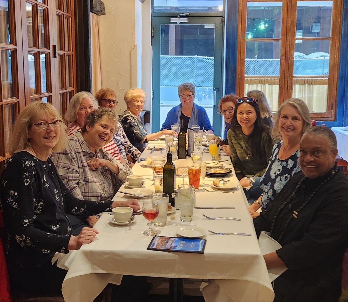 Group of people seated around a long dining table in a bright restaurant, smiling at the camera