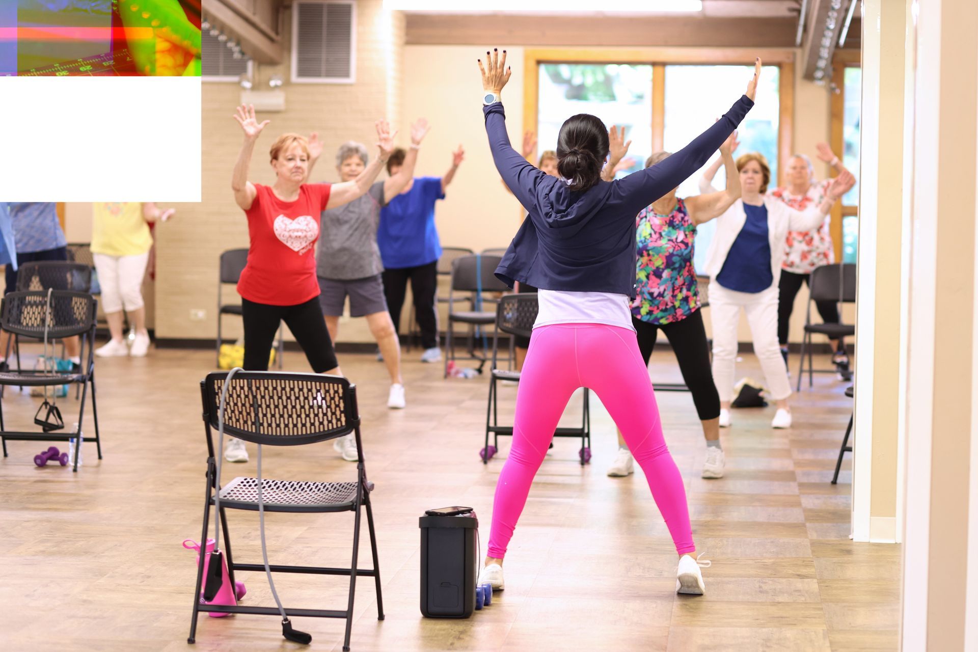 Fitness class in a studio, participants raising arms while facing an instructor in pink leggings