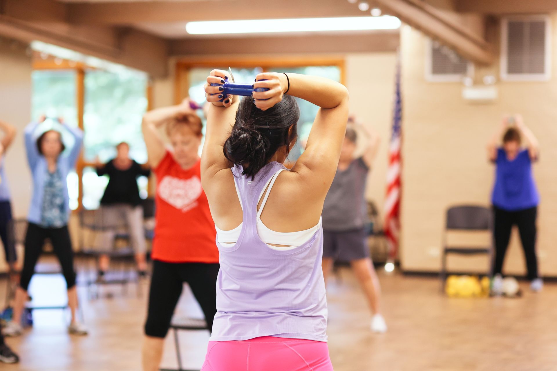 Fitness class with a woman stretching her arms overhead in a bright studio, others exercising in the background