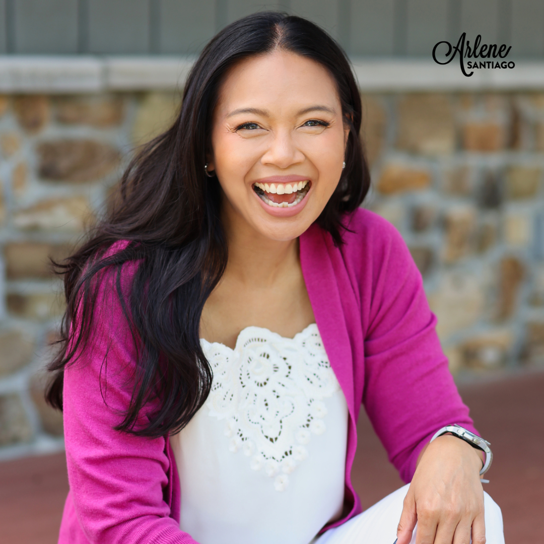 Smiling woman in a magenta cardigan and white top seated outdoors before a stone wall