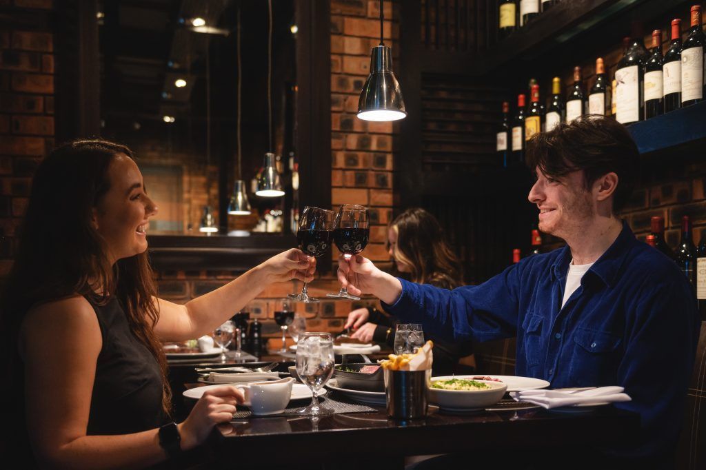 Mann og kvinne på restaurant skåler og smiler under en date. Hvem betaler?