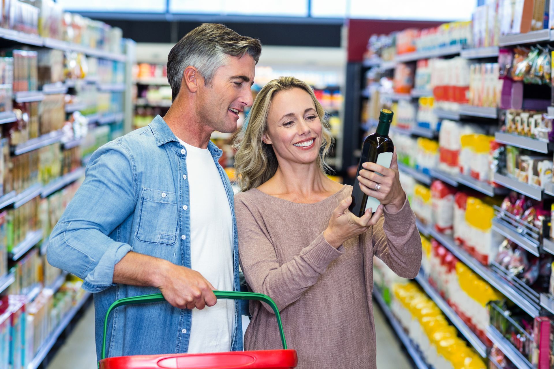 Couple shopping in a grocery aisle, smiling while checking a bottle on a phone