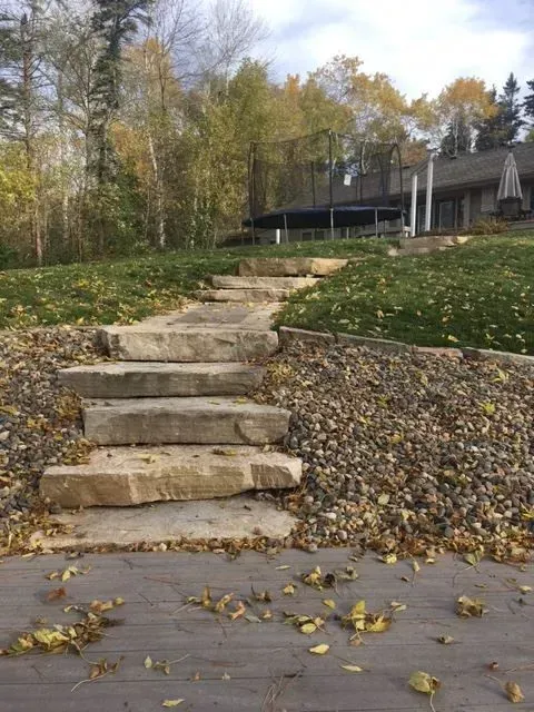 A stone walkway leading to a house surrounded by rocks and grass.