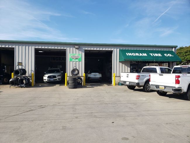Auto repair garage with open bays, cars inside, and white pickup trucks parked outside under a green awning.