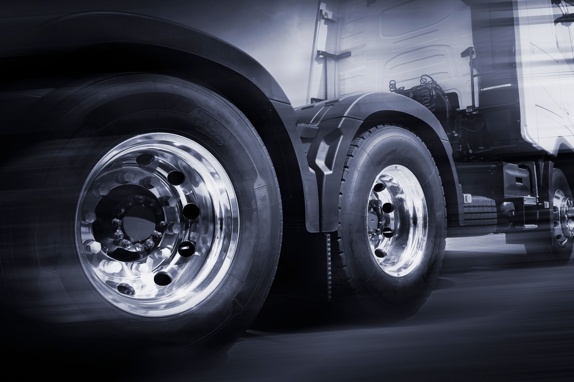 Close-up of a shiny truck’s rear wheels on a road, in a dark industrial setting