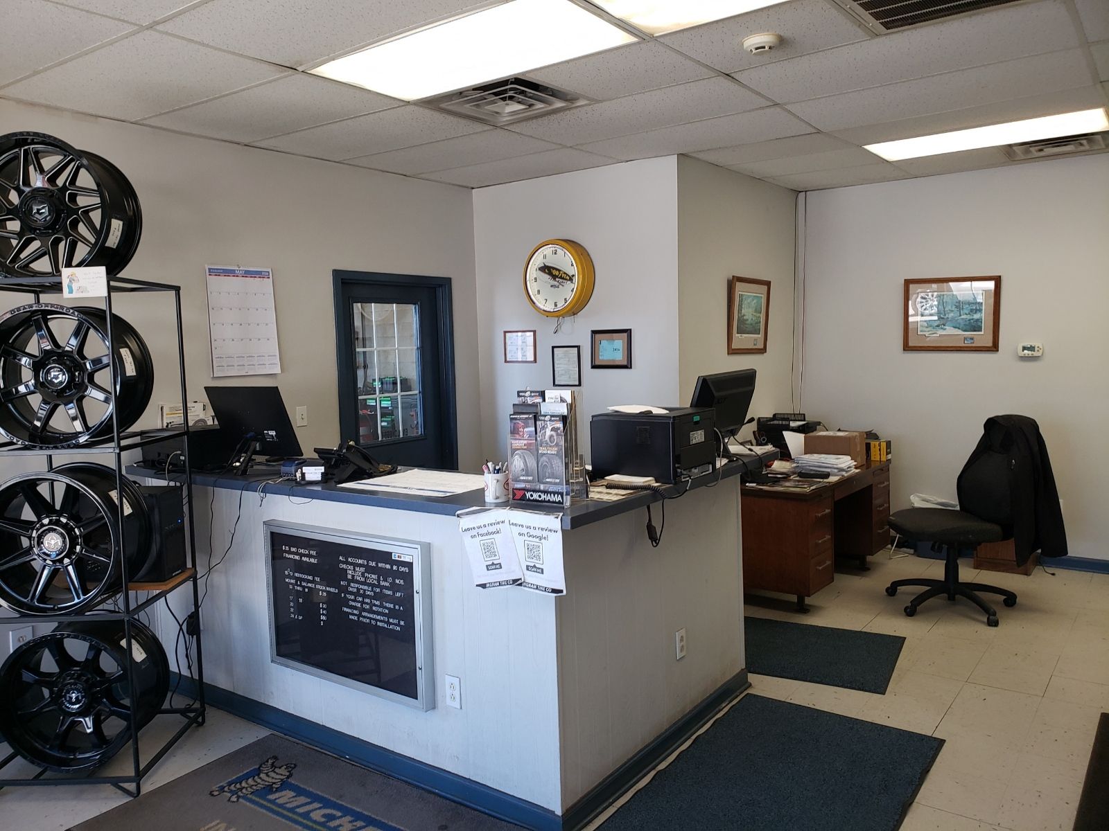 Office reception area with desks, computer monitors, wall clock, and framed pictures.