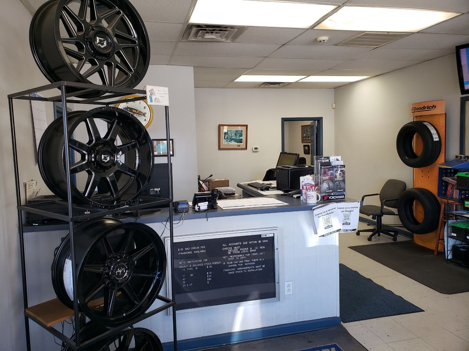 Automotive shop interior with stacked black wheels, a front counter, and tires on the right wall.