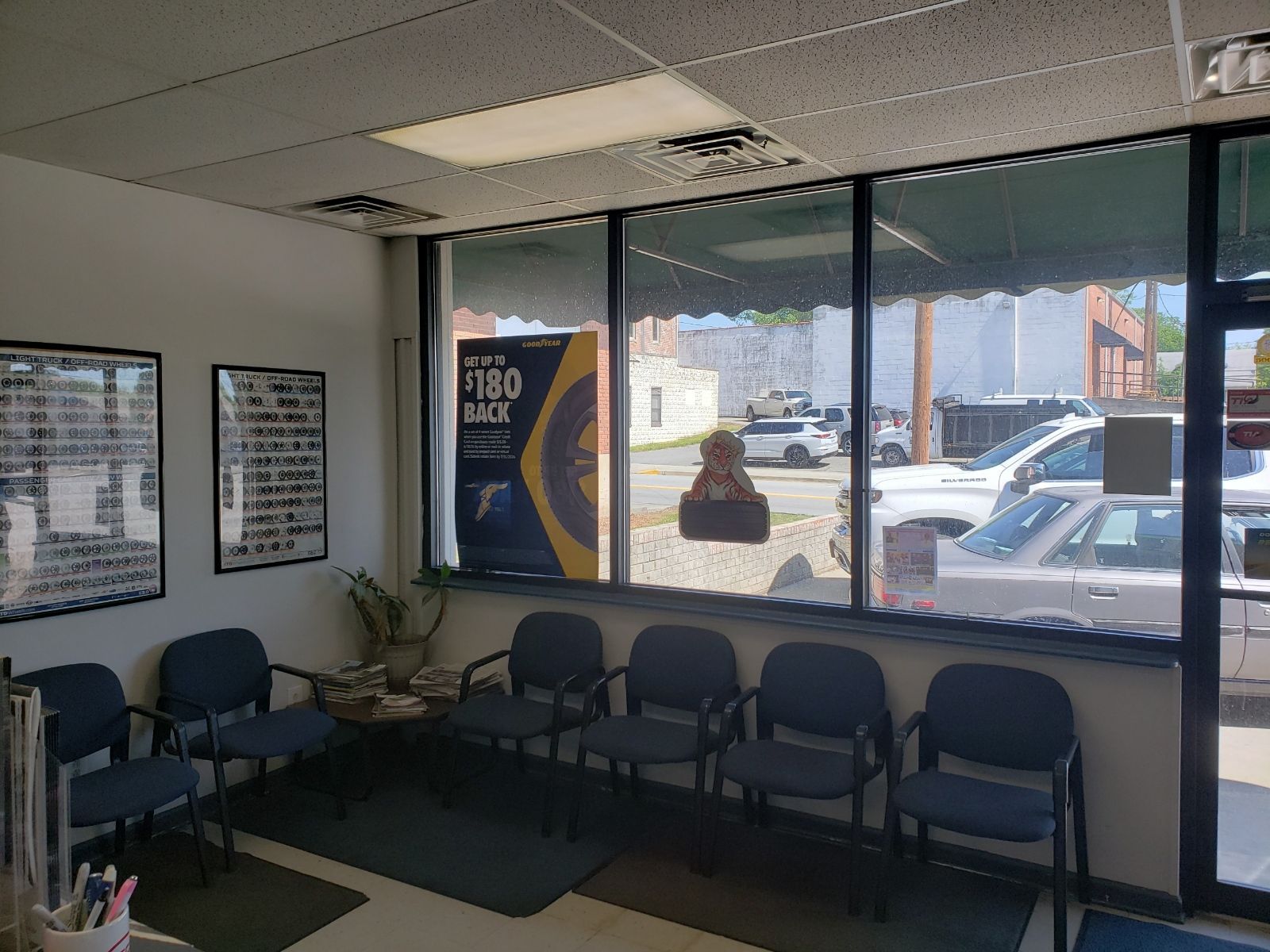 Empty waiting room with blue chairs, a black couch, and large windows showing parked cars outside