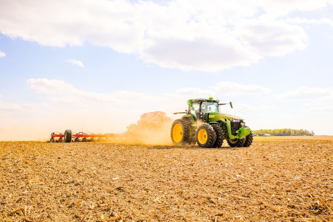 Green tractor plowing a dusty field under a bright sky