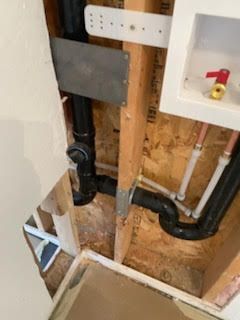 Plumbing pipes inside a wall cavity. Black drain pipes, copper water lines, and a red water shutoff valve.