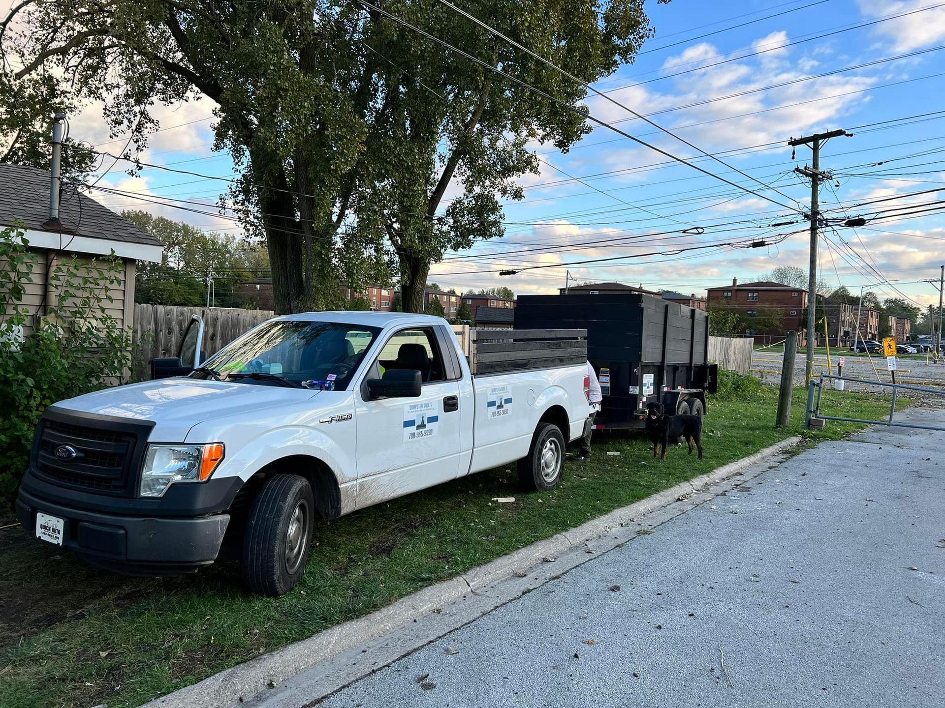 White pickup truck with a trailer parked on grass next to a road; in a residential area. The sky is overcast.