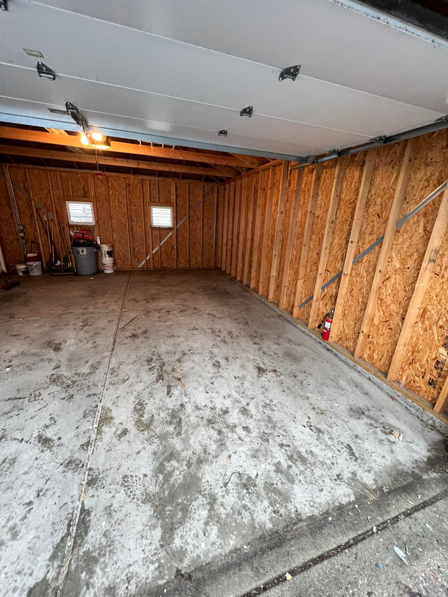 Interior of an unfinished garage with a concrete floor and exposed wooden walls. The garage door is open.