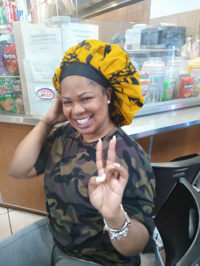A woman wearing a camouflage shirt and a yellow bonnet is giving a peace sign.