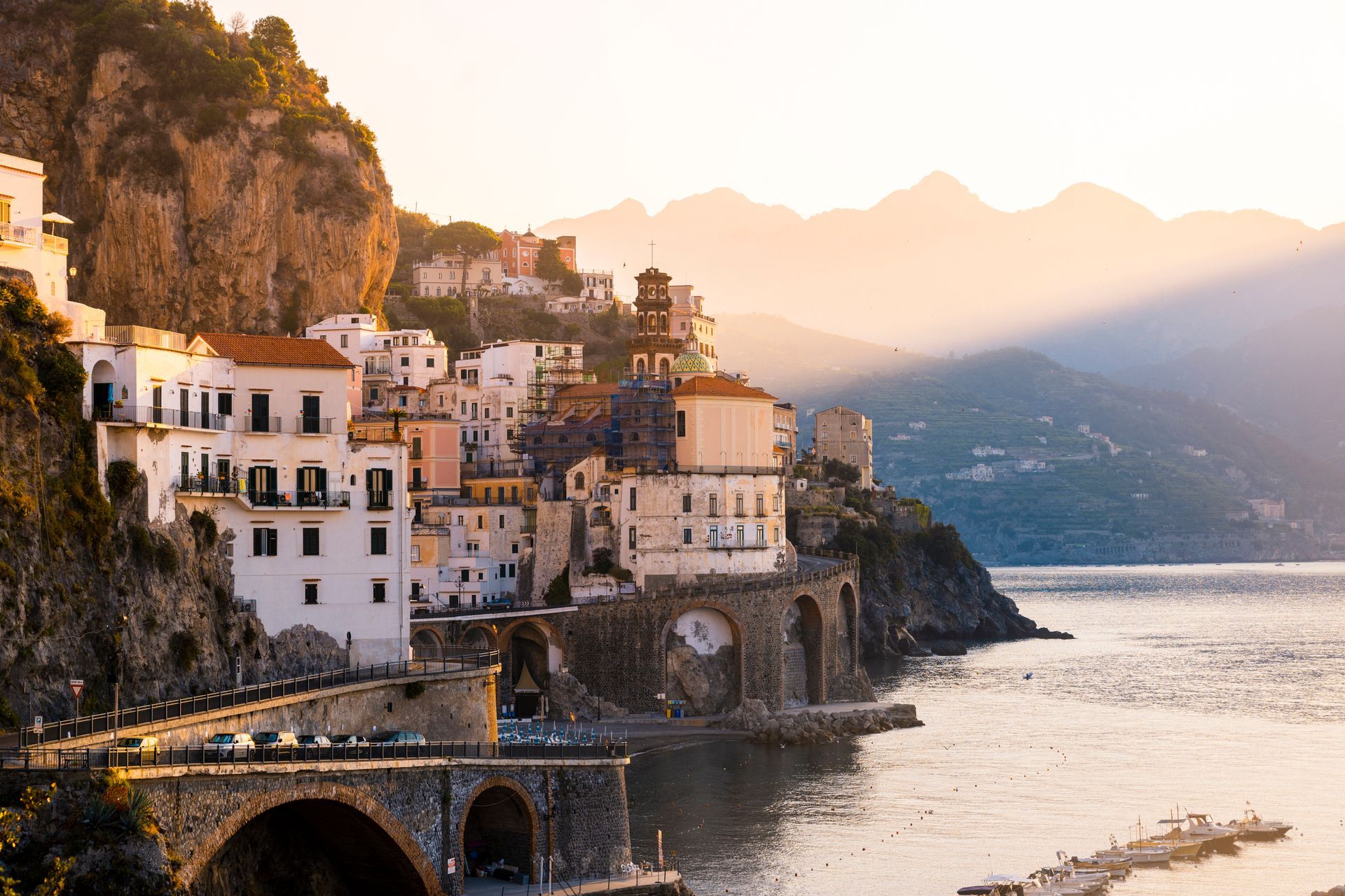 Una piccola città su una scogliera che domina uno specchio d'acqua con le montagne sullo sfondo.
