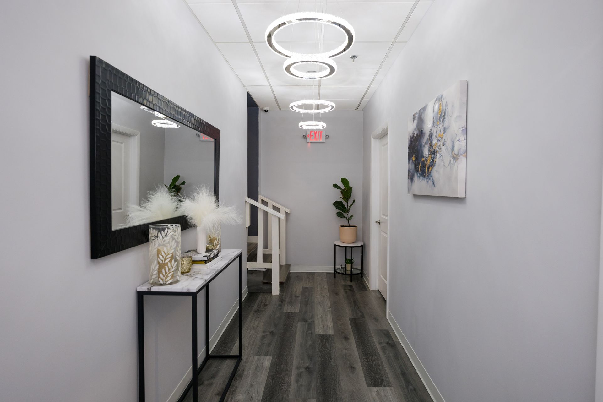 Narrow modern hallway with wall mirror, console table, chairs, plant, and circular ceiling lights.