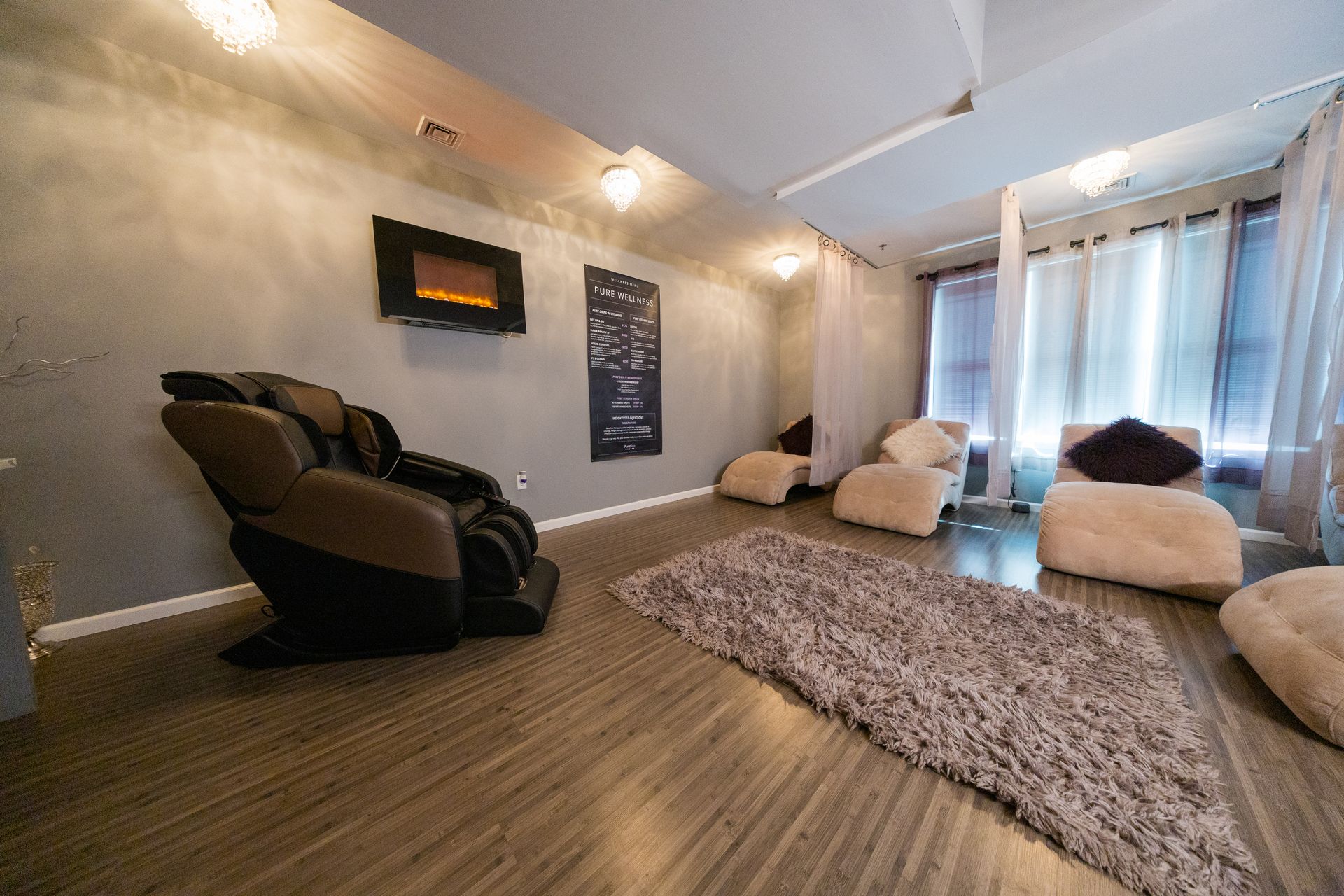 Cozy living room with reclining chairs, shag rug, soft lighting, and sheer curtains by a bright window.
