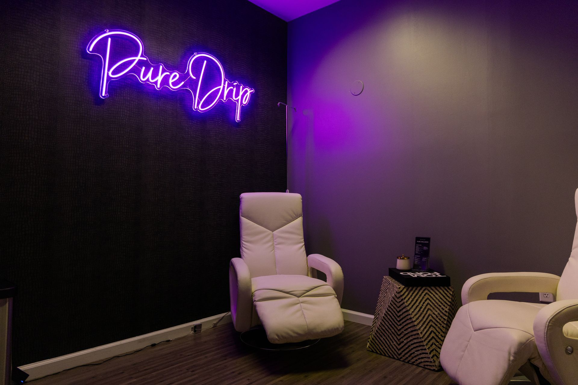 Purple-lit wellness room with massage chairs, a small table, and a neon sign on the wall