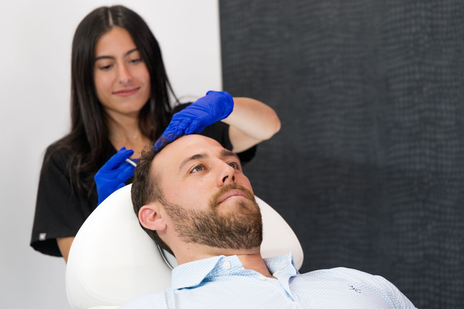 Woman in blue gloves applying a treatment to a reclining man in a clinic