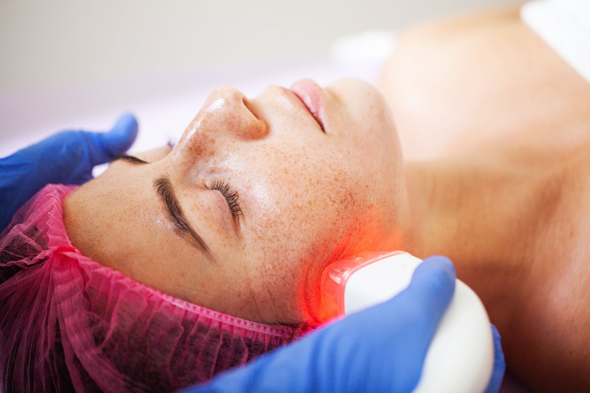 Gloved hands using a glowing treatment device on a person’s face during a skincare procedure