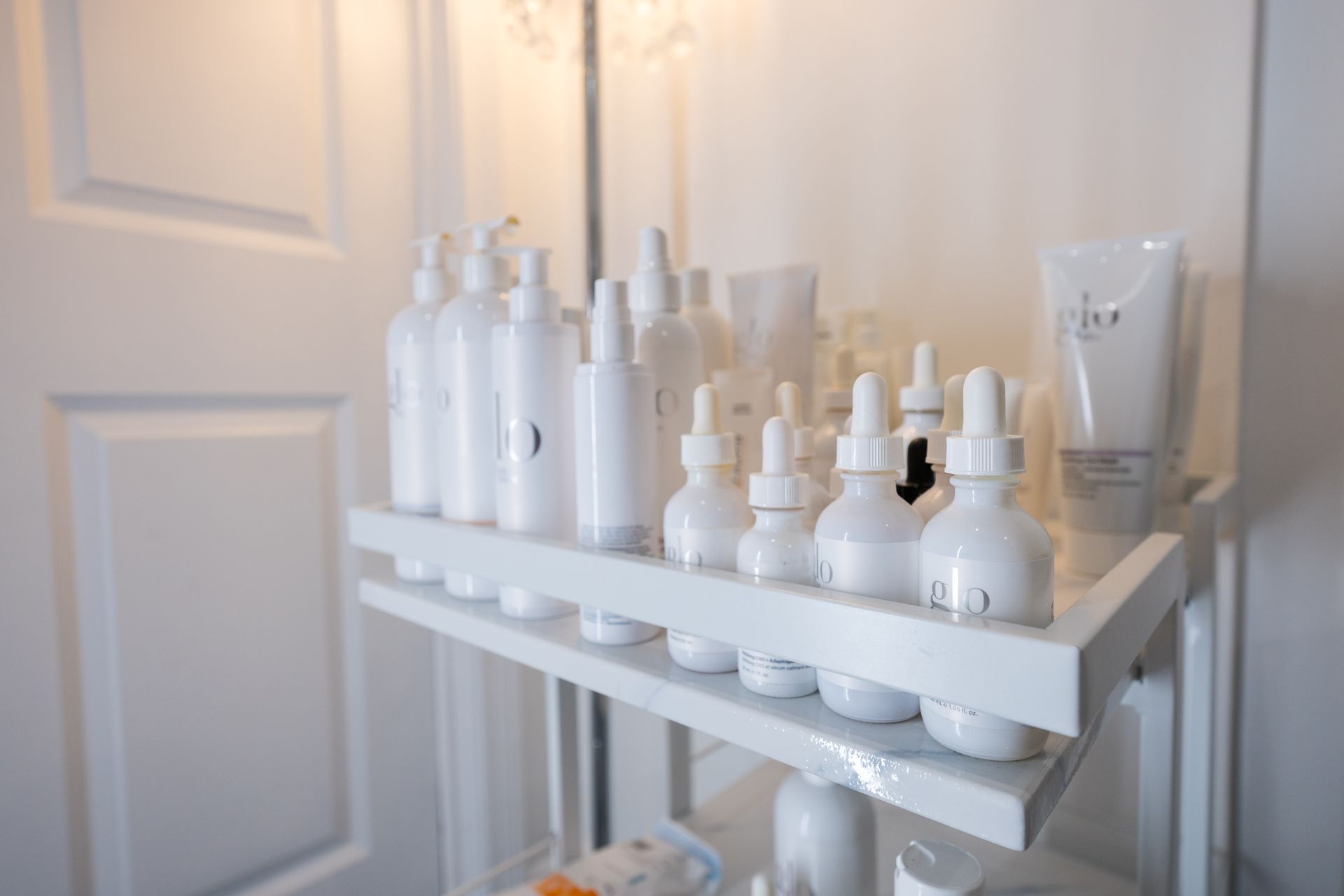 White bathroom shelf holding assorted skincare bottles and jars beside a closed door