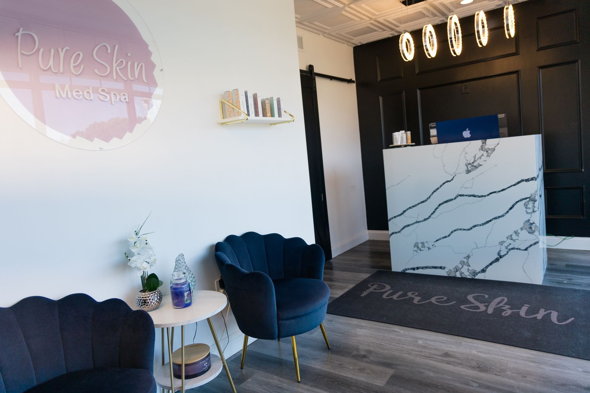 Modern salon reception with white marble desk, blue chairs, and “Pure Skin” wall logo