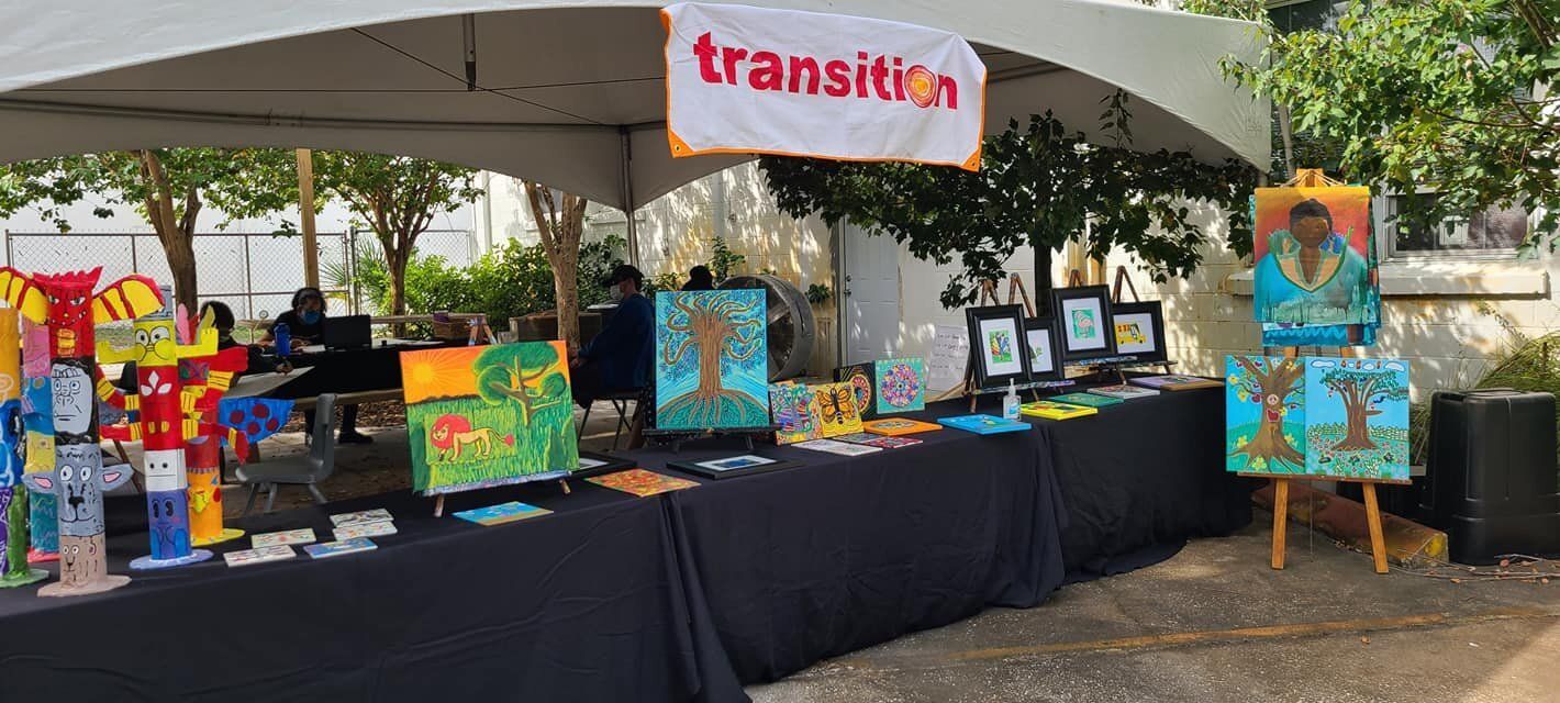 Art fair booth displaying colorful artwork under a tent.
