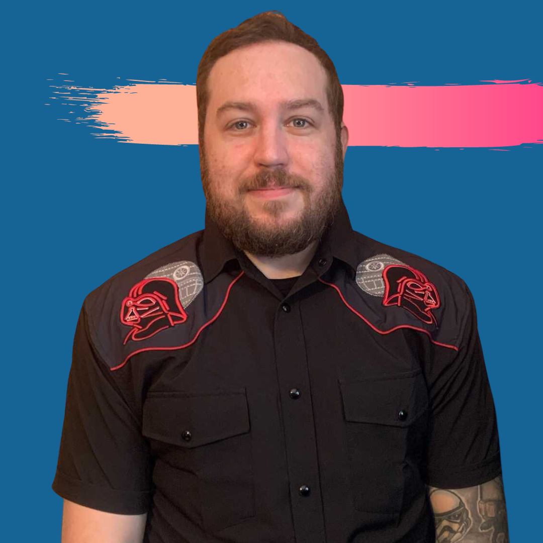 Man with beard in black shirt with red accents, standing against a blue background with pink and peach brushstrokes.