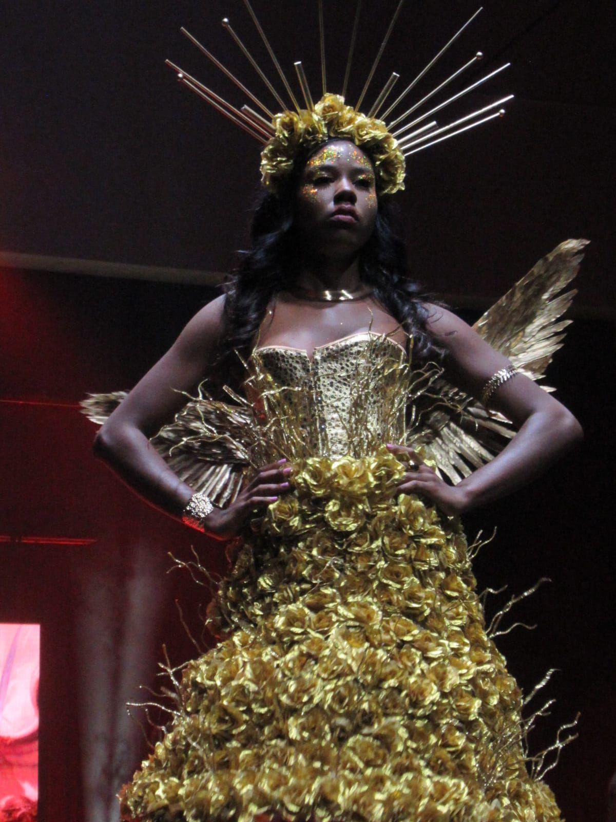 Woman in gold dress and halo posing on a runway.