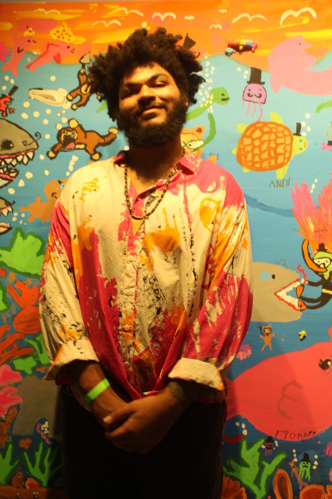 Man with beard smiles, standing in front of colorful mural with underwater characters.