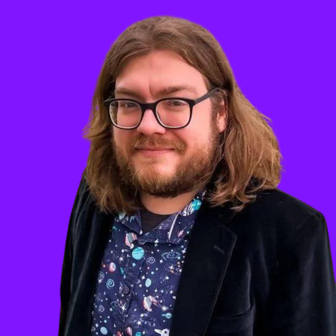 Man with long brown hair and glasses, wearing a blazer and a space-themed shirt, smiling against a purple background.