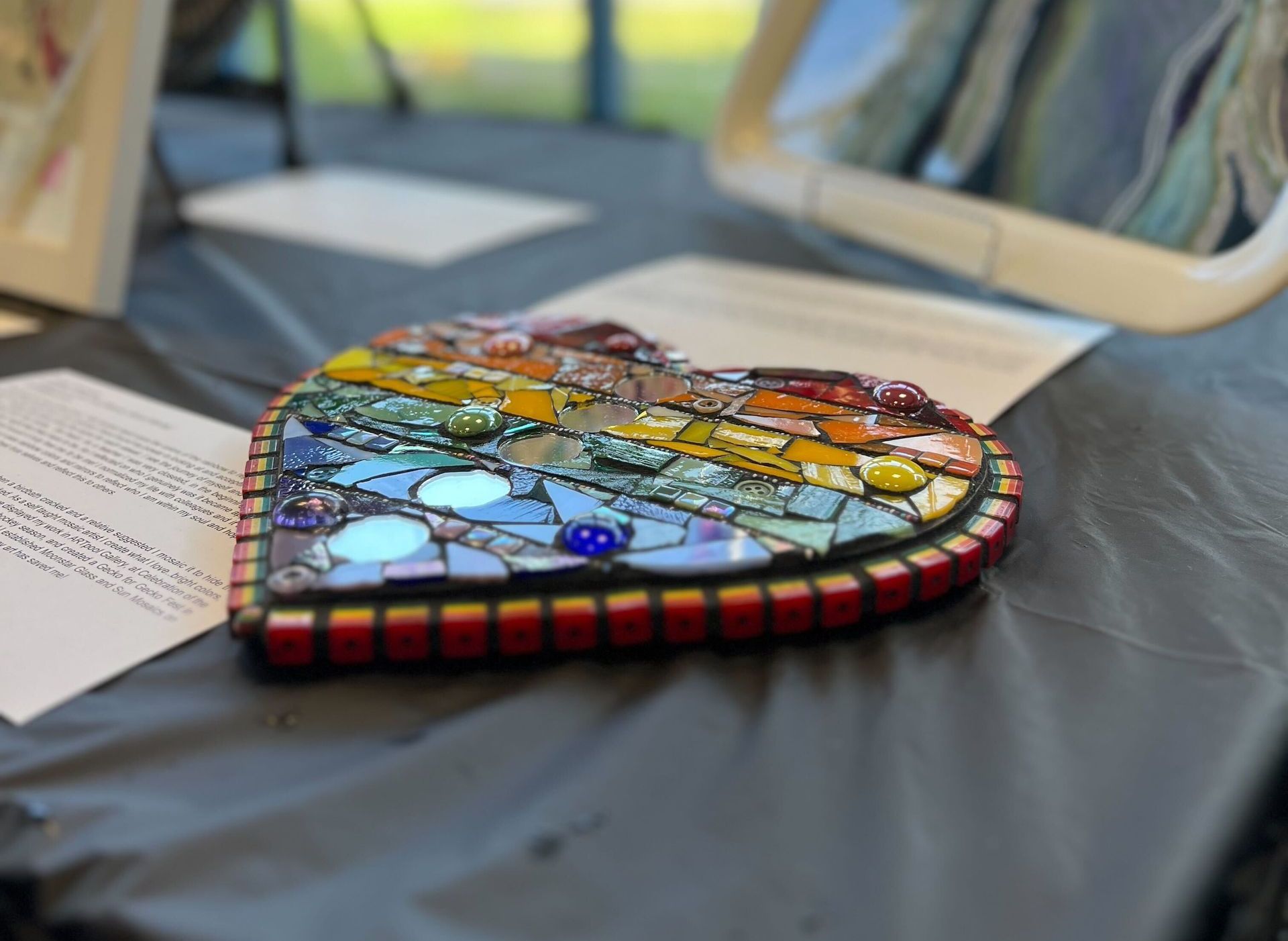 Mosaic heart art in rainbow colors on a table, with papers.